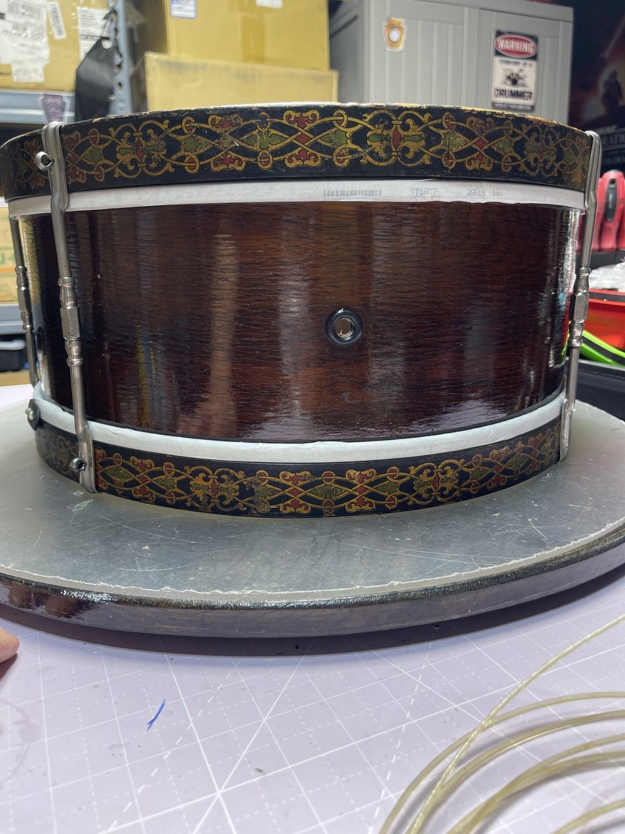Antique 1905 Harmony snare drum with ornate gold and red inlaid band decoration on a dark wood shell